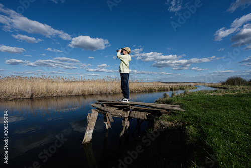 Tableau sur toile Young person observing marshland with binoculars from a rickety wooden dock unde