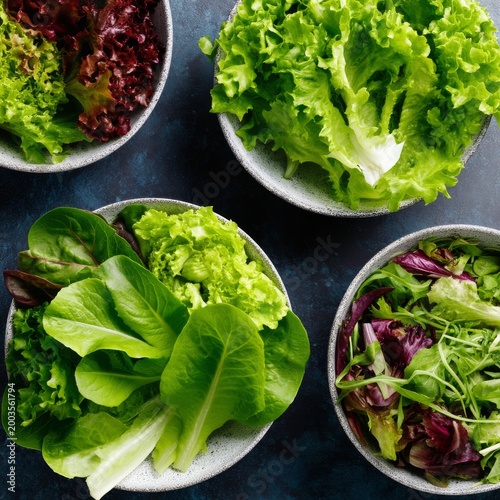 Fresh Salad Greens in Bowls on a Dark Surface With Natural Light in a Kitchen...