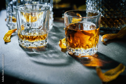 Elegant whiskey pair in crystal tumblers with glowing amber drink, dramatic shadows and yellow floral accents for premium bar and restaurant branding