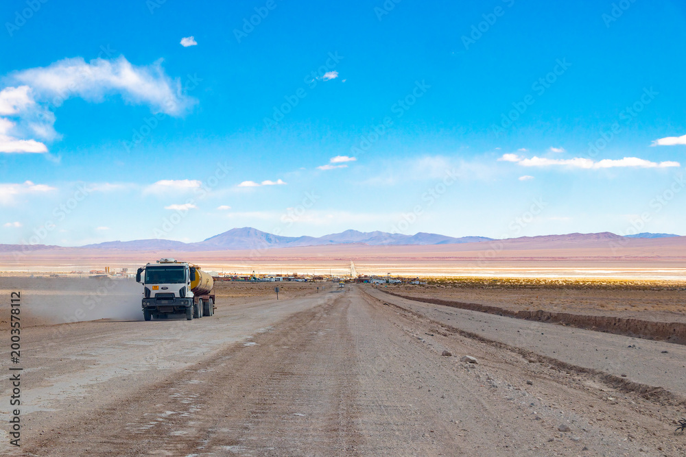 Fototapeta premium Heavy industrial truck driving on a dusty gravel road in the Puna de Atacama desert near Tolar Grande, Salta, Argentina. Logistic transportation