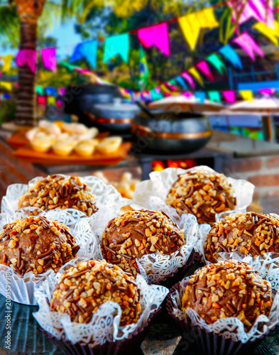 Traditional Brazilian Paçoca brigadeiros topped with peanuts and chocolate sprinkles at a Festa Junina celebration. Festive background with colorful flags and rustic typical food.