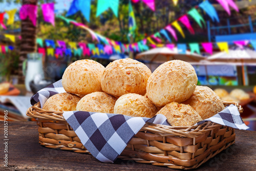 Canvastavla A basket of freshly baked Brazilian cheese bread (Pao de Queijo) on a rustic wooden table, featuring a festive Festa Junina background with colorful flags and decorations