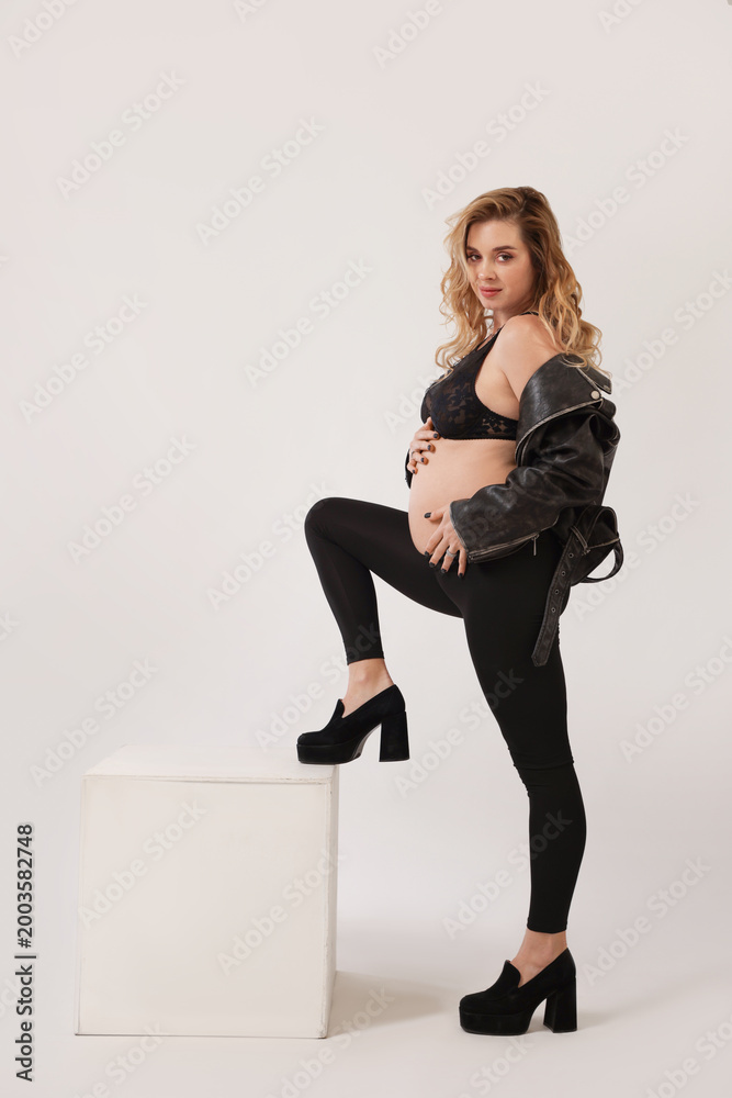 Fototapeta premium Beautiful pregnant woman in stylish outfit posing on light background