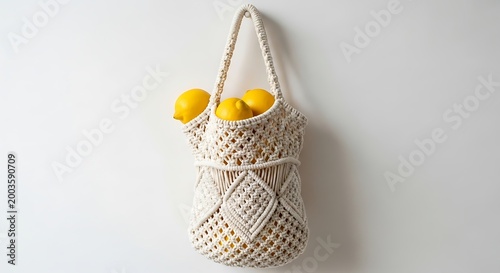 Handmade macrame market bag filled with fresh yellow lemons hanging on a white wall, showcasing intricate knot patterns.