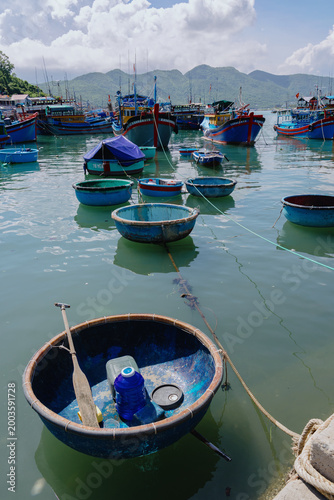 A fleet of colorful fishing boats are docked in a harbor in Hon Mieu, Nha Trang, Vietnam. The traditional basket boats are also visible in the foreground.