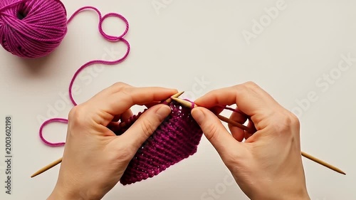 Close-up of hands knitting with purple yarn and needles on white background.