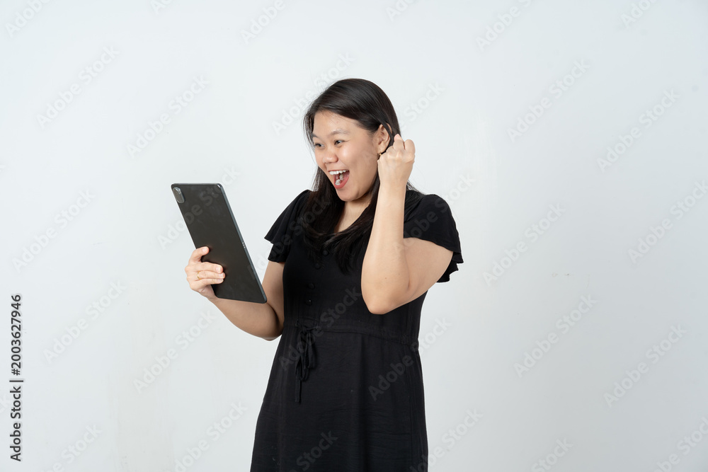 Naklejka premium Cheerful Asian woman celebrating success while looking at tablet screen