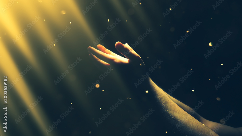 Fototapeta premium A man's hand reaches out to the shimmering divine rays of bright golden light in the darkness. The concept of religion, God, soul, faith.