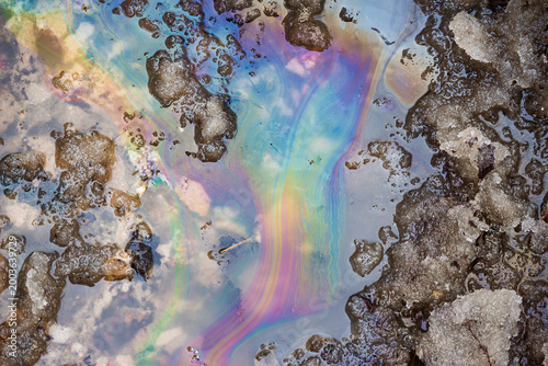 Colorful oil slick on melting snow puddle, spring thaw, environmental pollution, abstract texture