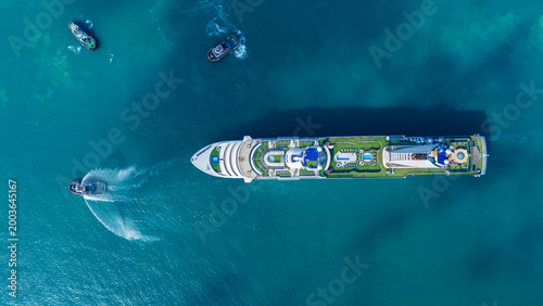 Tableau sur toile luxury cruise ship escorted by three tugboats in clear turquoise ocean water