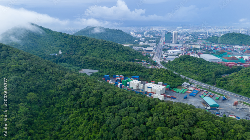 Obraz premium inland container depot and logistics yard nestled in lush green mountains next to a busy highway. Urban city skyline and foggy hills in the background. Sustainable transport.