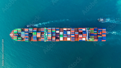 Fotografija container ship fully loaded with colorful cargo containers being assisted by tugboats in the open sea