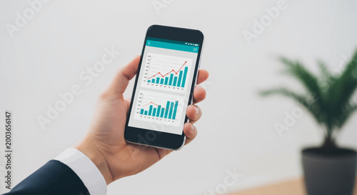 Man holding smartphone displaying financial stock market charts and graphs.