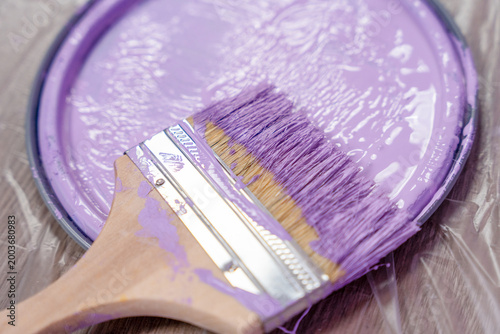 Close up of a paint brush loaded with pastel lavender paint over an open can, highlighting wet texture, home decorating work and a soft colored renovation concept in detail