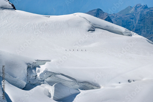 Photos Group of mountaineers crossing glacier ridge in alpine mountains, minimal landscape and vast snowy terrain