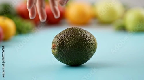 A hand gently holding a fresh, ripe, green avocado, ready to be prepared for a healthy meal on a light blue surface