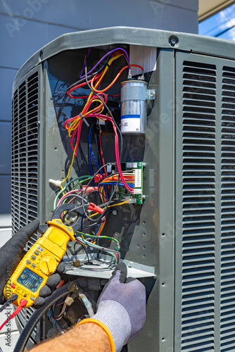 Fotografía HVAC technician using a clamp meter to measure load current on an outdoor AC uni