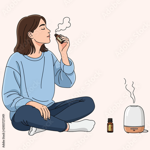 Woman sitting on floor smelling essential oil bottle with ultrasonic aroma diffuser nearby.