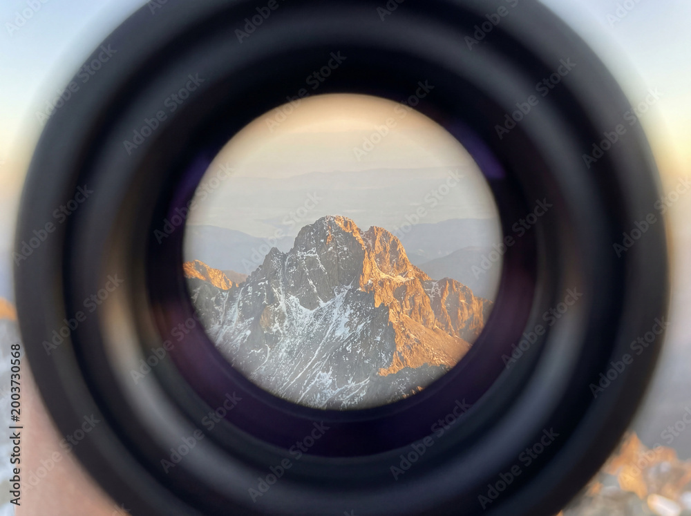 Naklejka premium POV through a telescope blurred edges focusing on a distant mountain peak touched by light
