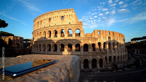 Ancient Roman Colosseum landmark stands majestically bathed in golden hour light with a modern smartphone resting on a stone foreground offering a travel technology contrast