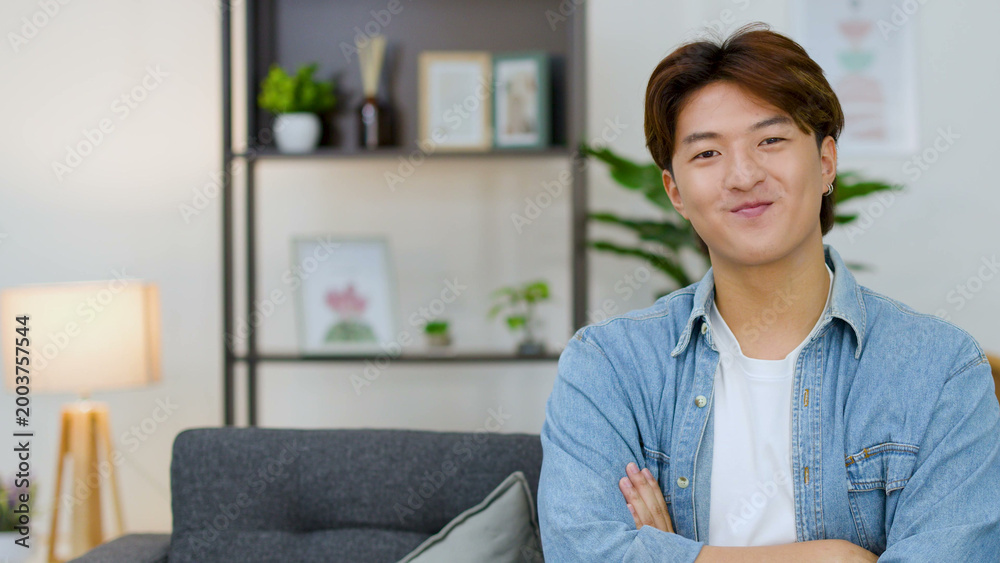 Fototapeta premium Smiling Young Asian Man with Arms Crossed in Modern Living Room