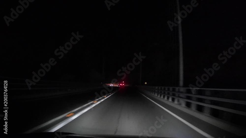 Dashcam point of view driving at night on a highway. Visible road markings, traffic signs and car lights ahead. Concept of transportation, road safety and night driving conditions.