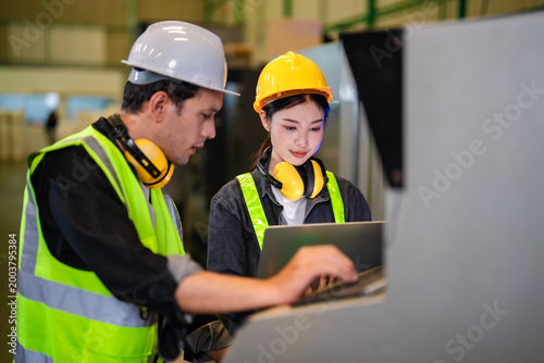 Technician showing laptop data to engineer beside industrial machine, collaborative analysis of production metrics and system performance in factory environment supporting data driven decision.