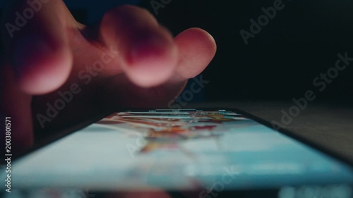 Mobile phone news scrolling at night. Macro view shows male hand browsing social feed on bright screen. Mobile phone use illustrates digital habits constant news checking and online media consumption.