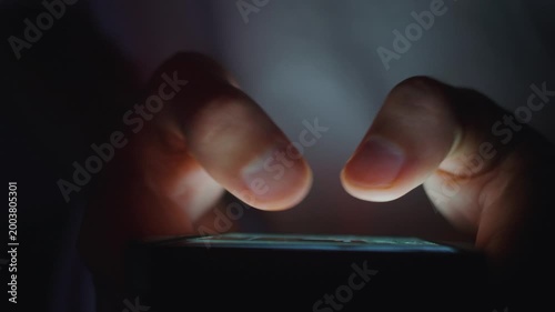 Smartphone in male hands with close up fingers tapping touchscreen while scrolling social media in dark mood. Smartphone use shows digital lifestyle online communication and modern mobile technology