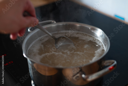Konstfotografi Water is boiling in a pot on a kitchen stove as a person stirs with a spoon