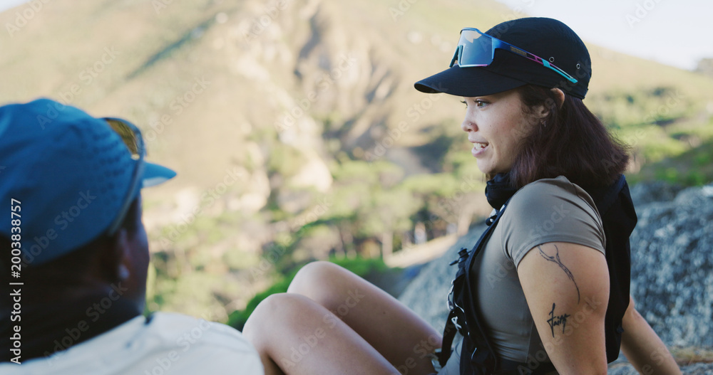 Fototapeta premium Outdoor, couple or woman with break for travel, hiking adventure discussion or tourism for holiday. Relax, talking and people with trekking trip for vacation, interracial and sightseeing in nature