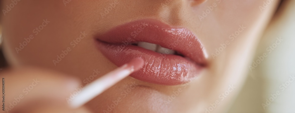 Naklejka premium Woman applying lip gloss with a brush in softly lit setting 