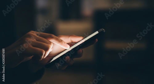 Close up of hands using smartphone in dark room, person browsing mobile phone at night, glowing screen light on finger and touchscreen device