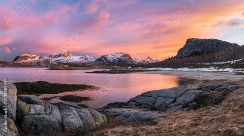 Mountains covered in snow rise above a quiet coastal bay during a dramatic pink and orange sunset sky event.