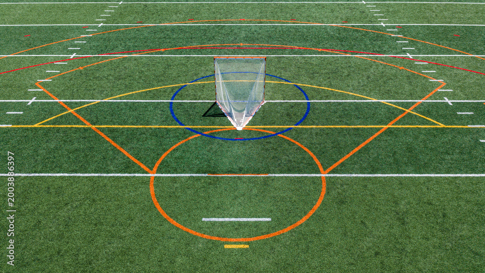 Fototapeta premium Aerial view of a multi-purpose athletic turf field featuring a lacrosse goal within a blue circular crease and overlapping colored lines for different sports. Lacrosse, Soccer, Field Hockey, Football