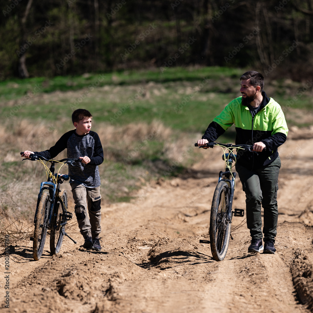 Obraz premium Father and son enjoy a bike ride on a sunny day, along a sandy trail.