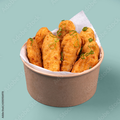 Tableau sur toile Fried chicken wings with crispy coating and green onion garnish served in paper
