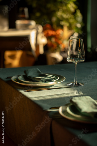 Stylish restaurant table with plates wine glass and folded napkin in warm sunlight creating cozy dining atmosphere