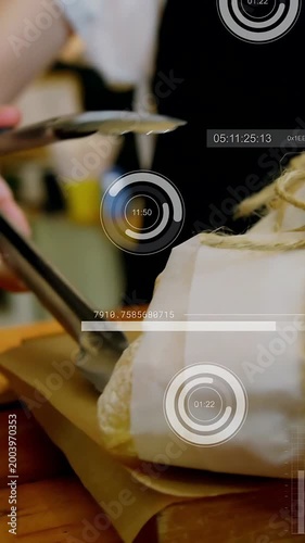 Vertical video: Hand with tongs nearing and adjusting twine-wrapped sandwiches for display with HUD