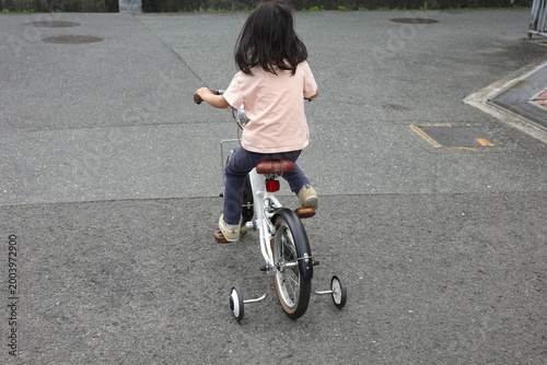 Back View of a Little Girl Riding a Bicycle with Training Wheels