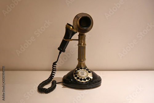 A classic black and brass vintage candlestick telephone with a rotary dial, placed against a minimal white background.