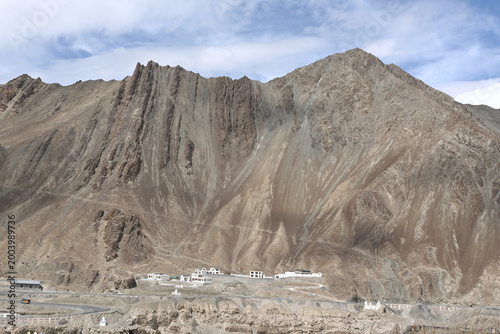 A massive, rugged mountain towering over a small village in a barren valley.