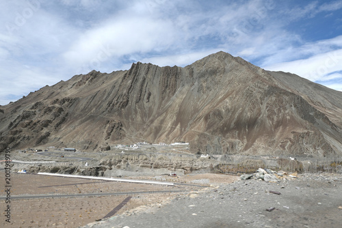 A massive, rugged mountain towering over a small village in a barren valley in Ladakh,India.