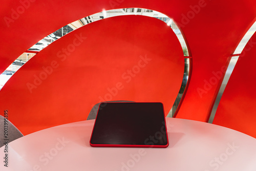 Digital Tablet with Blank Screen on White Table in Front of Modern Red Abstract Architectural Backdrop