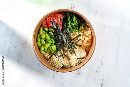 Fresh tuna poke bowl with edamame, chukka, nori, and sesame seeds in a craft box on white marble. Top view of premium gourmet takeout food.