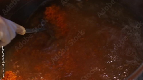 Ingredients simmer in a boiling pot as a rich soup mixture is stirred. The scene highlights the cooking process, bubbling texture, and careful preparation in a professional kitchen environment.