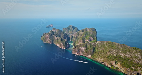 Tropical Phi Phi island displaying lush green limestone cliffs rising from turquoise water with boat cruising past, offering a stunning travel destination and vacation landscape. Aerial drone panorama
