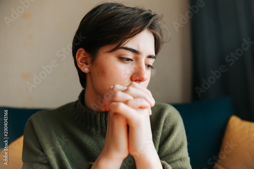 Canvas Print A young woman with short hair is sitting indoors with her hands clasped together, appearing thoughtful