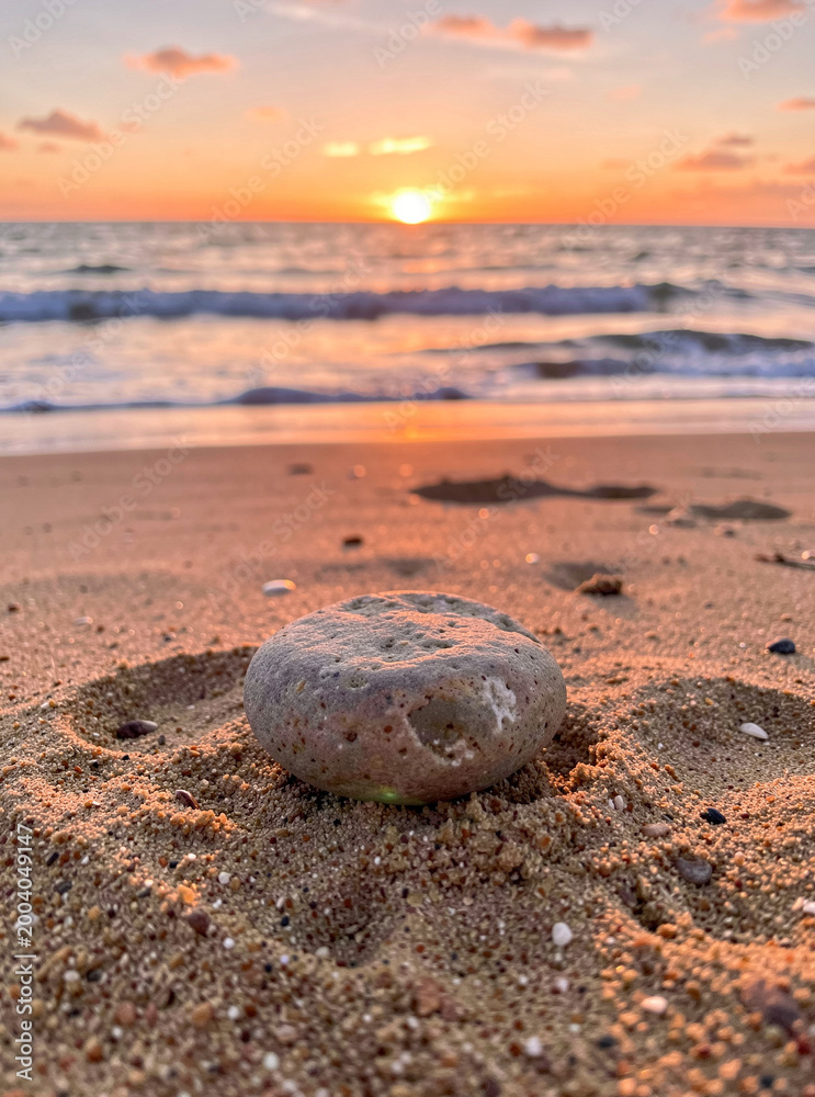 Fototapeta premium A serene beach scene at sunset with a single rock in focus.