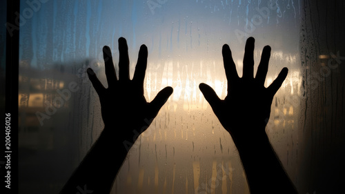 Dark silhouettes of hands against a steamy window pane with vertical rain streaks at sunset